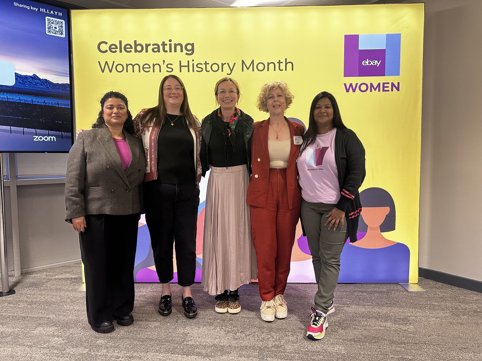 Five women smiling together at a corporate event celebrating Women's History Month