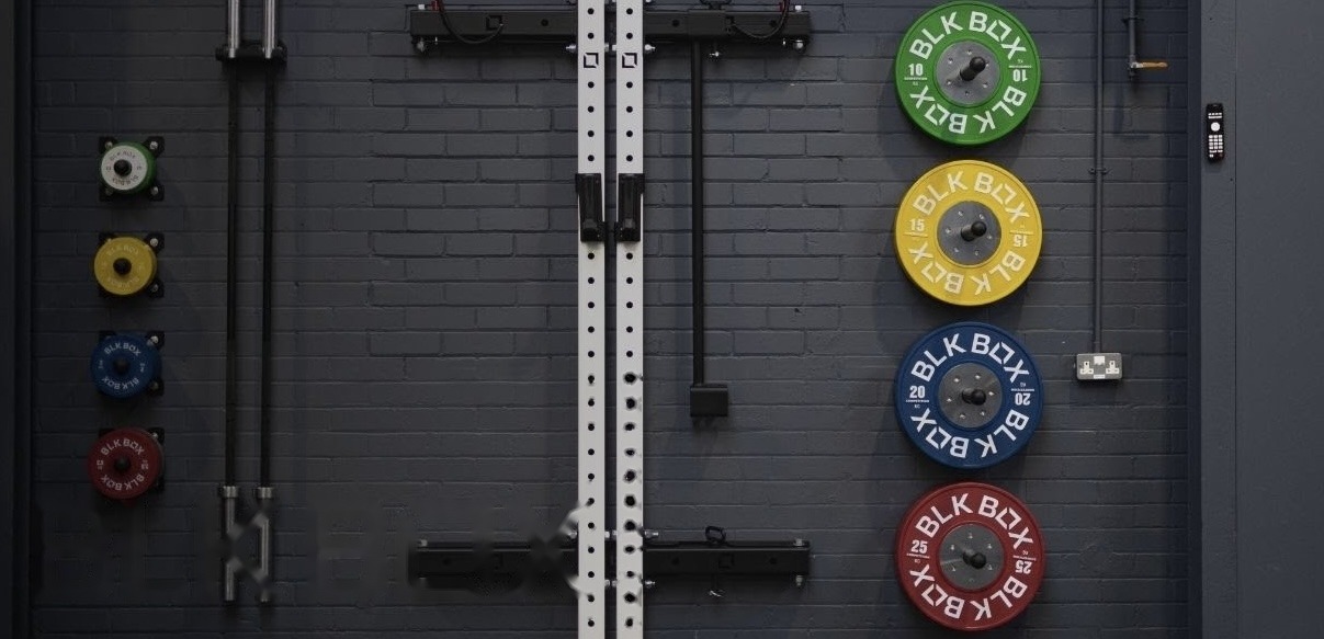 Wall-mounted plate storage, barbell holders and rig attachments — an example of the space-efficient equipment layouts used in a Titan Wellness fit-out
